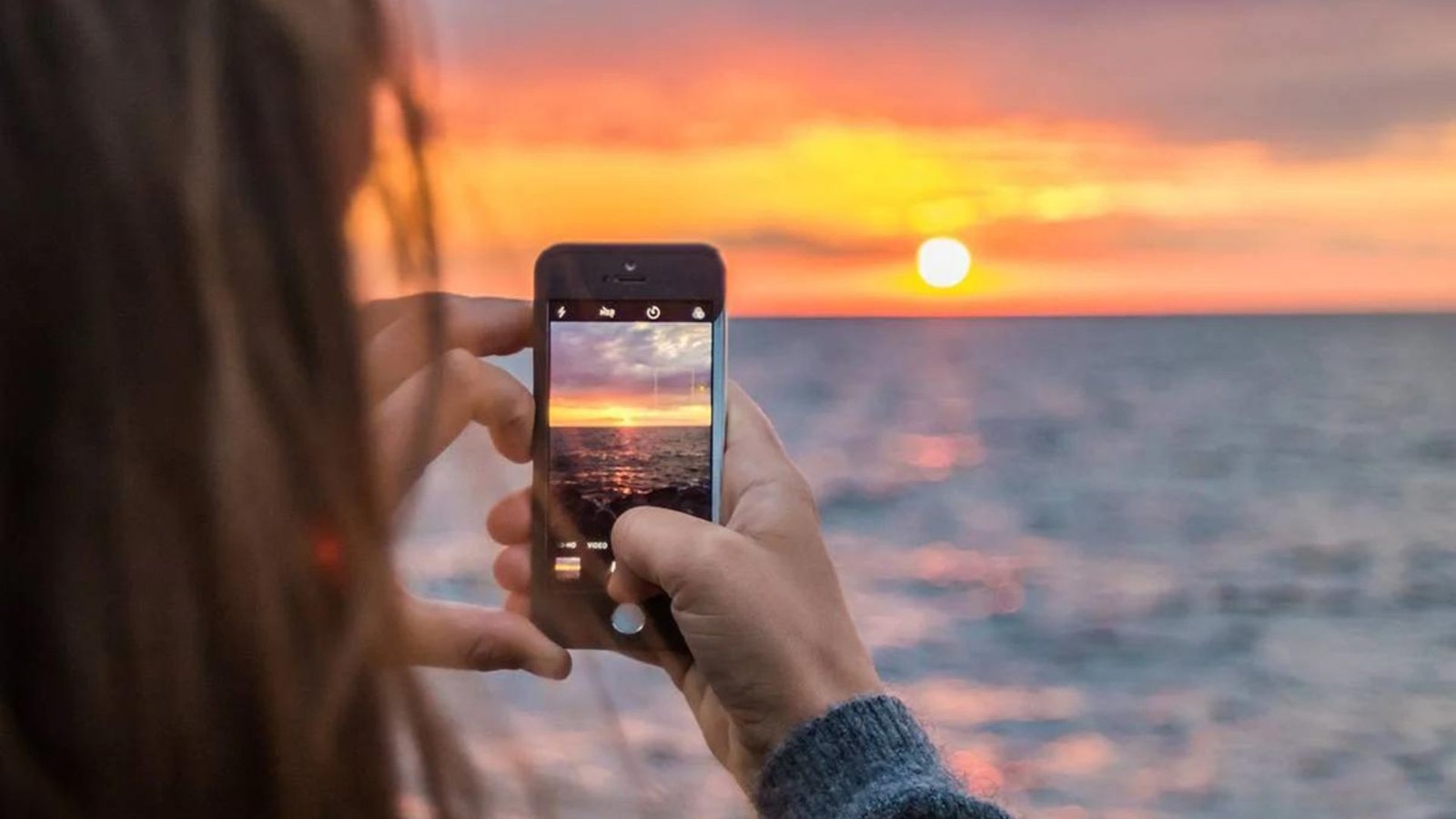 A Picture of a Woman Taking a Looking at the Sunset  Holding a Phone Taking a Picture of the SunSet 